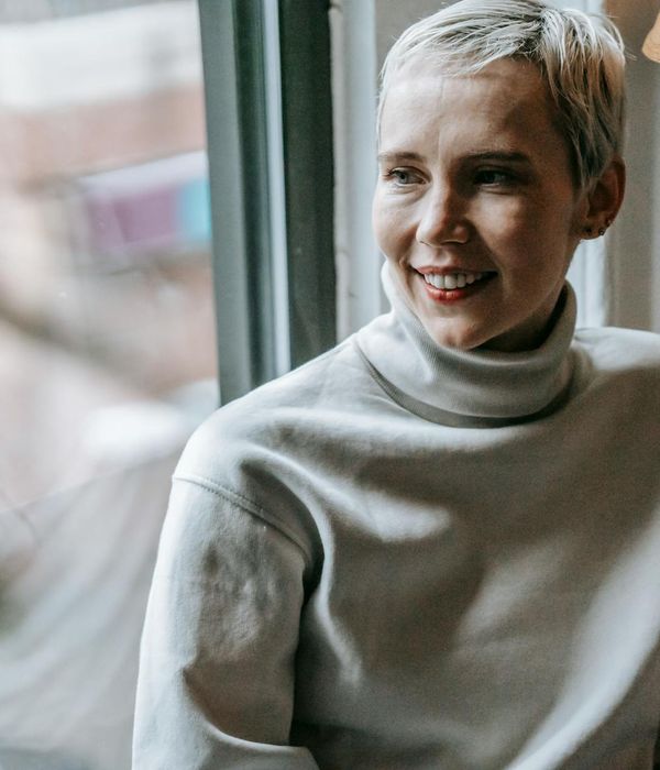Smiling woman feeling serene and confident in a bright room.